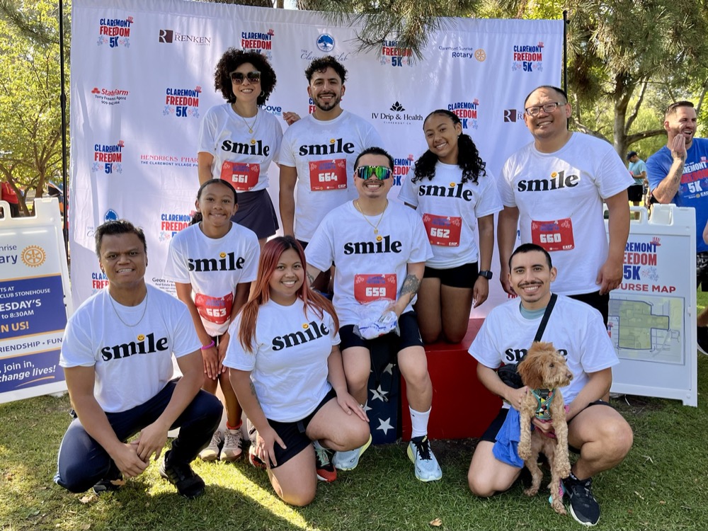 Baseline Orthodontics community members at the Claremont Freedom 5K marathon. A diverse group of runners wearing matching white "smile" t-shirts and race bibs smile for a group photo outdoors.